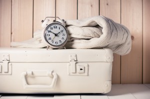 Beige knitted sweater, alarm clock and vintage suitcase on wooden background, retro decor